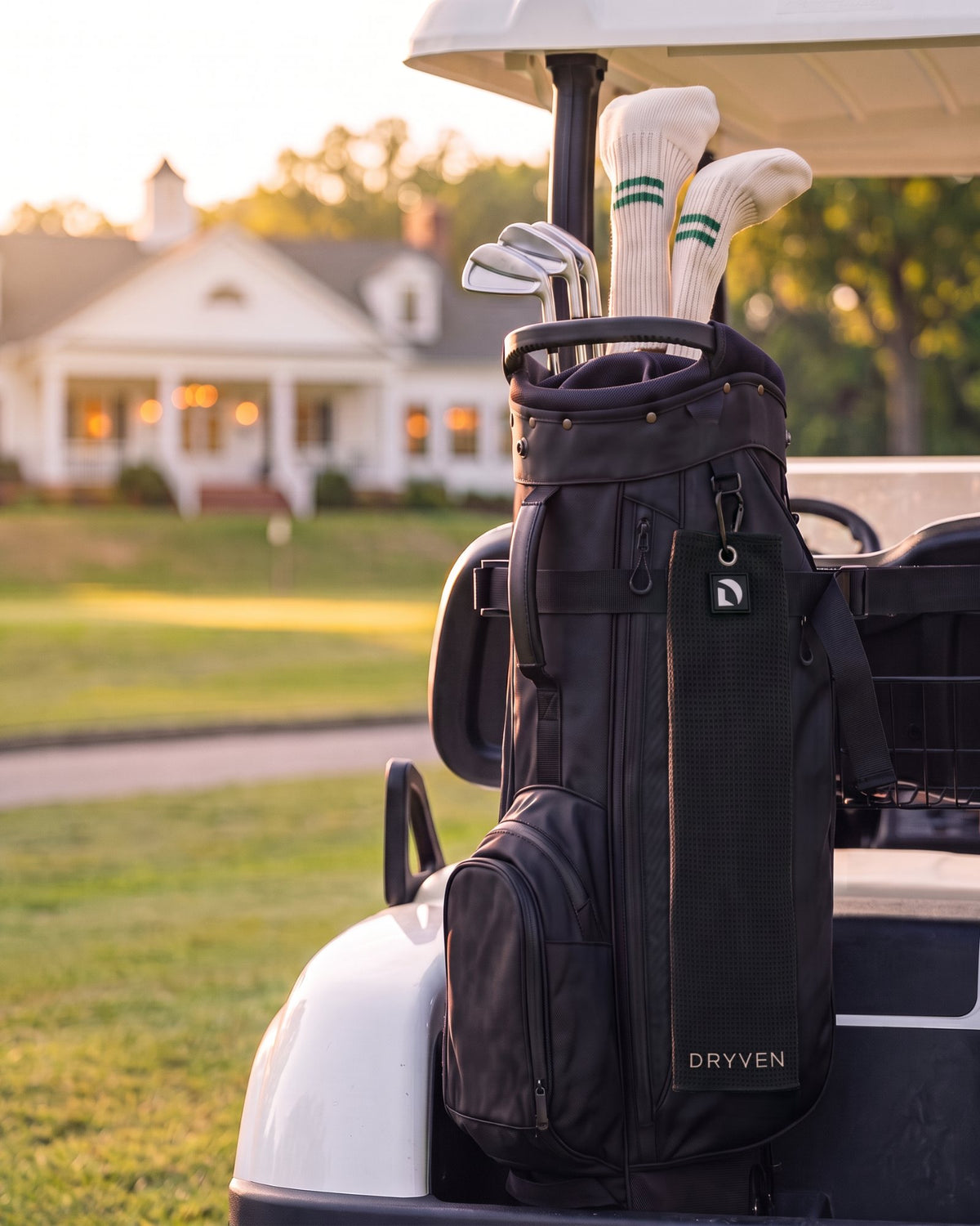 Golf bag on a cart at golden hour with the Dryven towel clipped on, clubhouse in the background