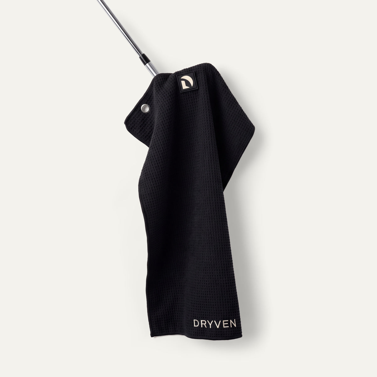 Black Dryven golf towel held by its magnetic logo badge against an iron head.