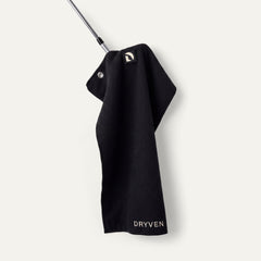 Black Dryven golf towel held by its magnetic logo badge against an iron head.